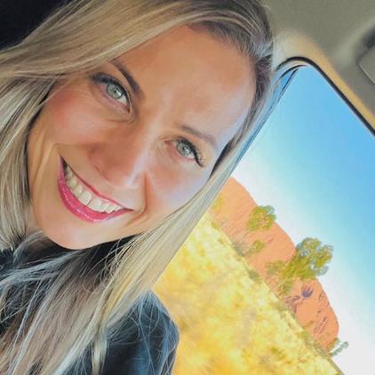 Stacey smiling brightly at camera with Uluru in  the background