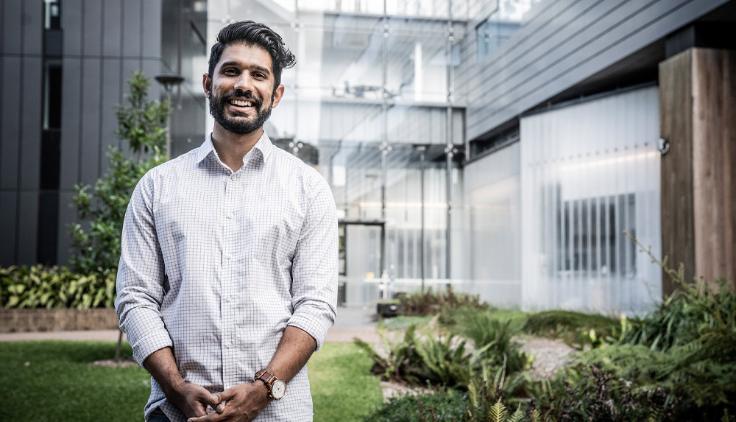 Anuk Indraratna standing in teh garden of Molecular Horizons, you can see the glass doors behind him