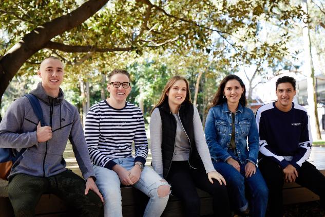 A group of UOWC students sit under a tree on campus