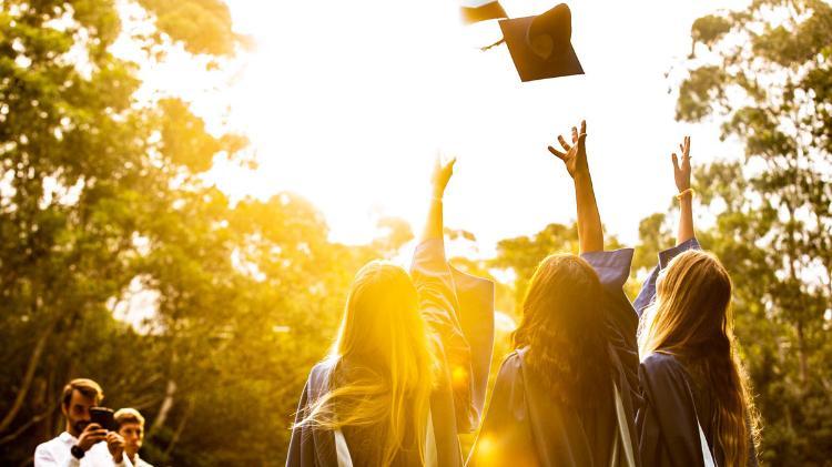 A group of UOW students celebrate autumn graduation by throwing their hats in the air