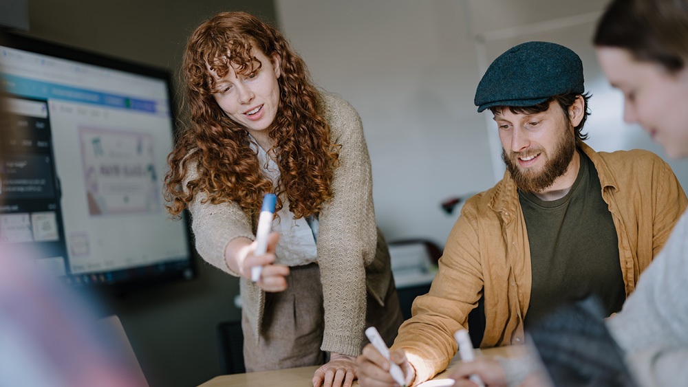 A team of 3 Bega students are working together on a project. The look of joy is evident on their faces. 2 of them are contributing to the poster paper with markers