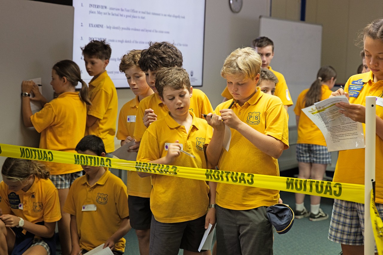 Primary age children, in school uniforms, at mock crime scene activity on campus