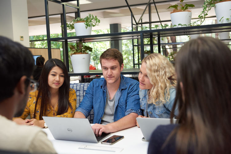 Students sitting together at a table working on laptops in a bright, modern study space.