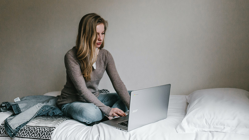 A female sitting on a bed with a laptop open