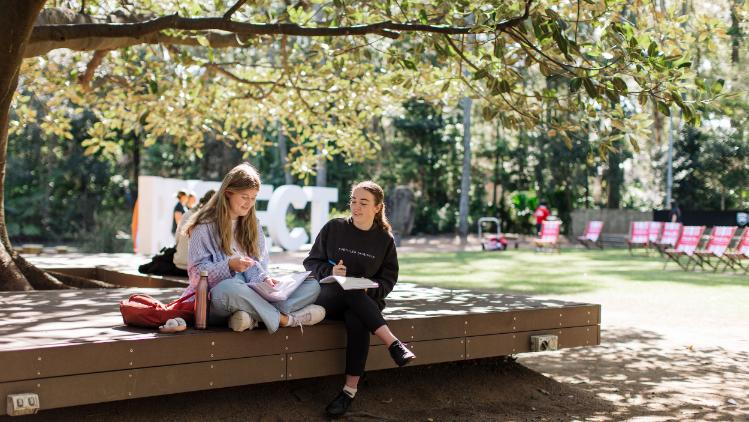 Students sit beneath a tree by the Duck Pond Lawn.