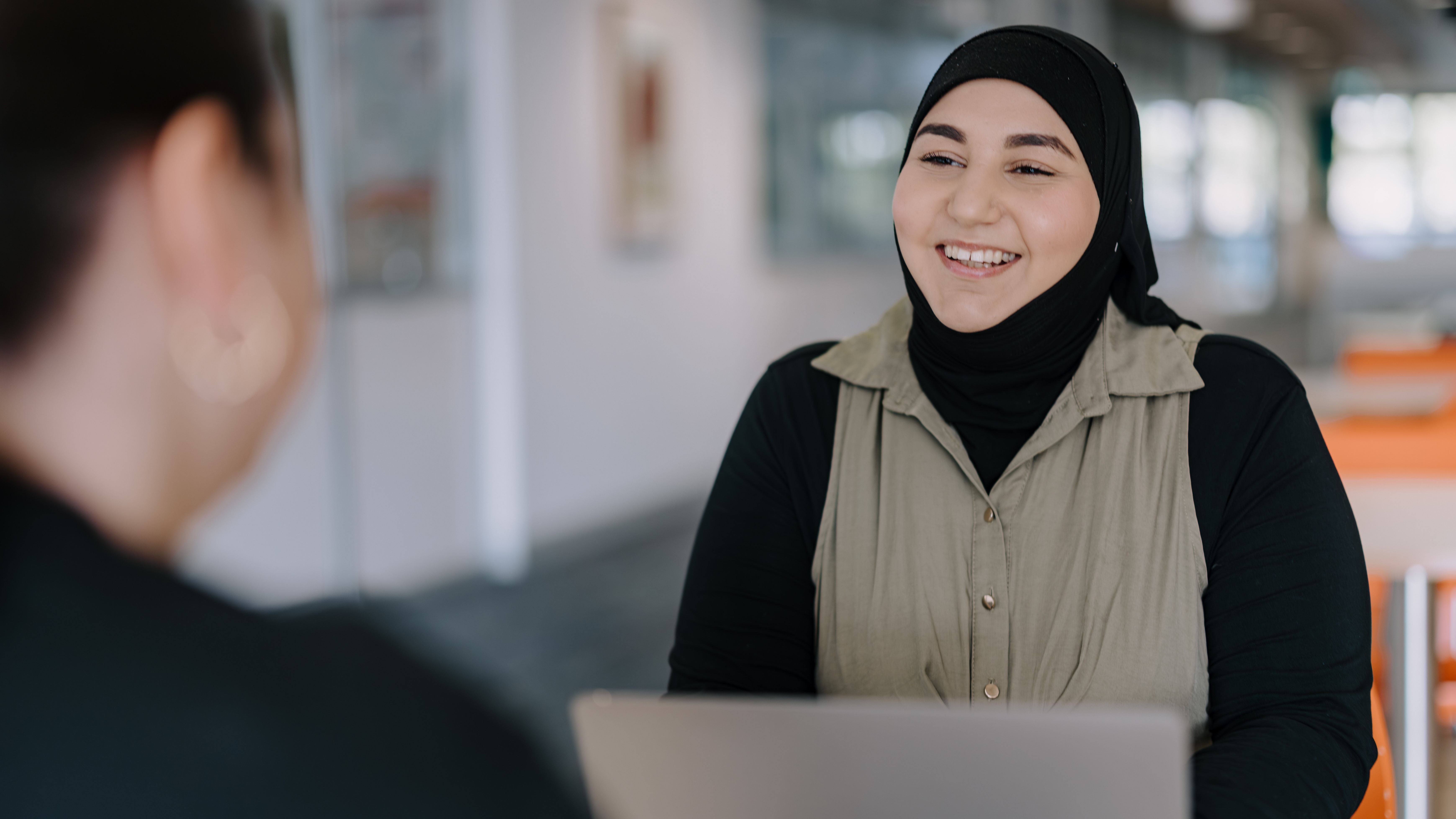 Two people sit across from each other having a happy discussion in an indoor office setting