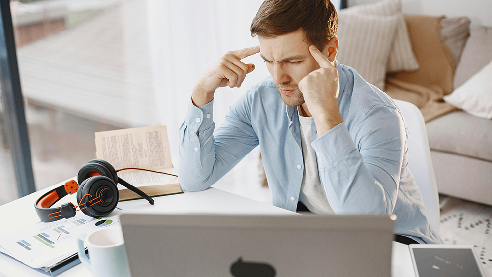 A male student sitting at a laptop looking stressed