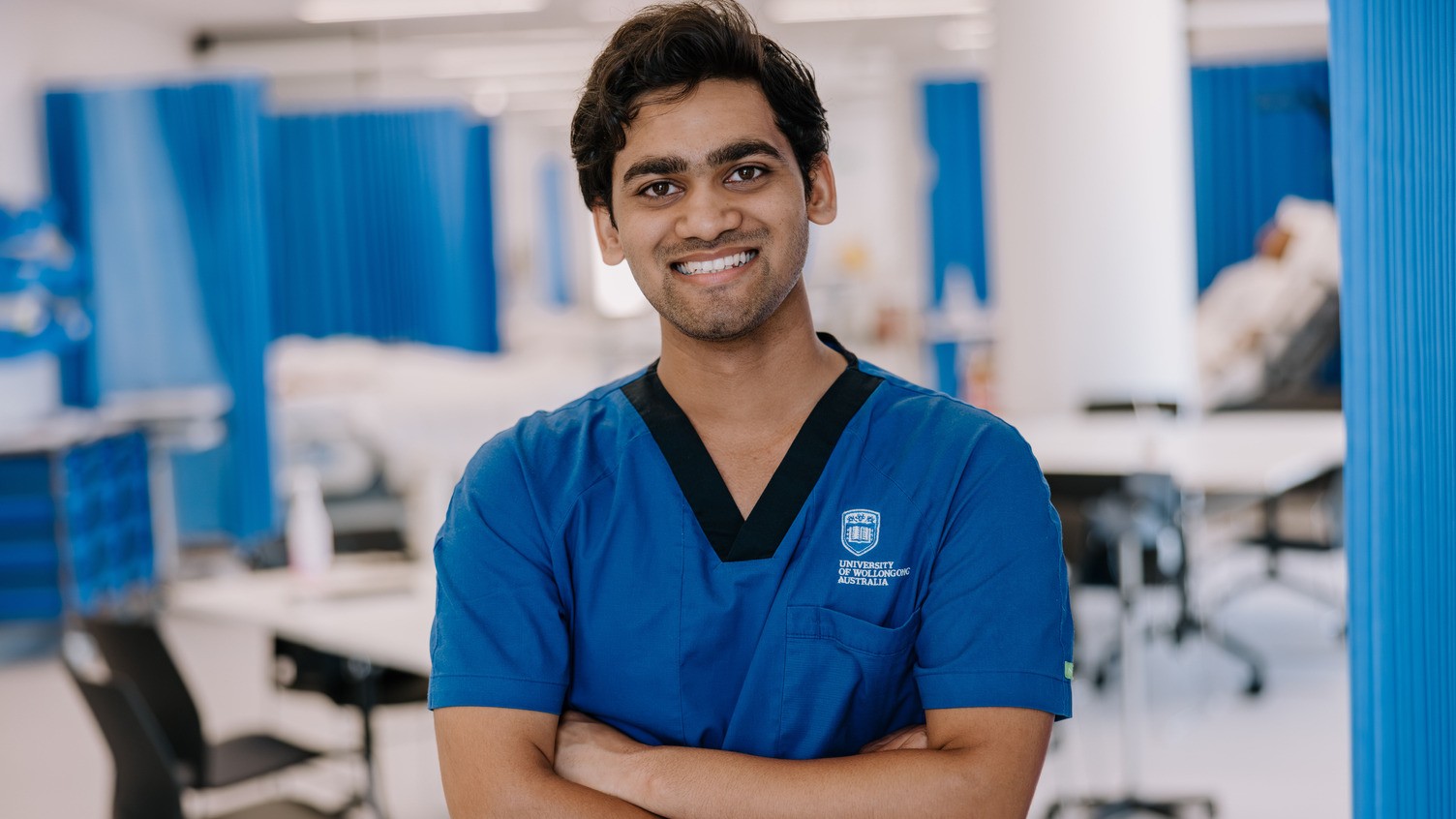 Student in University of Wollongong nursing uniform standing in a clinical training lab.  Provide your feedback on BizChat