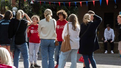 A group of people standing outside and being chatted to by people in red hoodies.