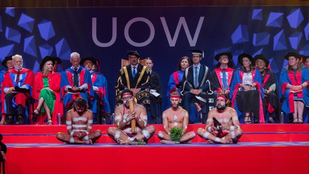 UOW graduation ceremony stage with a smoking ceremony in the foreground and academics in the background.