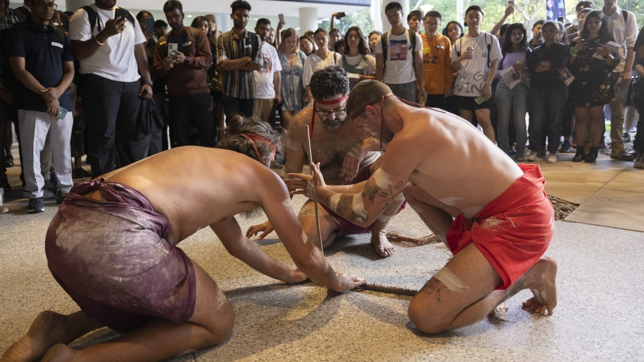 A group of Indigenous people are performing a smoking ceremony outdoors on the University of Wollongong campus during the Welcome to Wollongong event.