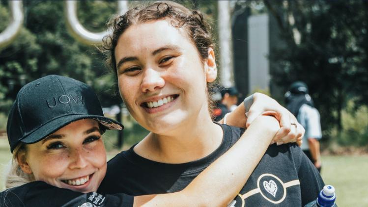 Two students smiling, one student hugging the other