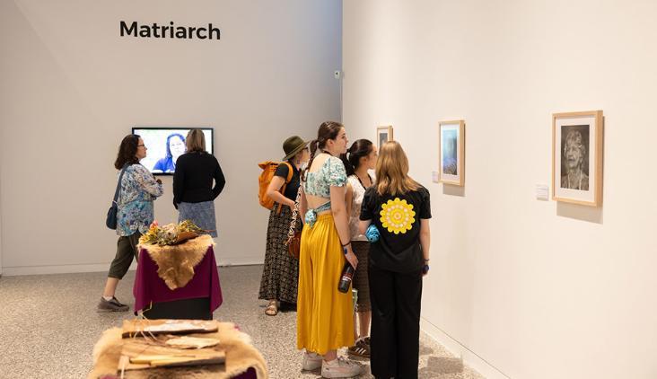 People stand in the white walled UOW Gallery and take in the artwork of Broc Piazza