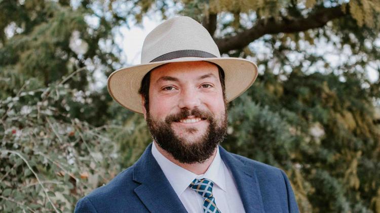 Dr Ronald Planer standing in front of trees in a wide brim straw hat