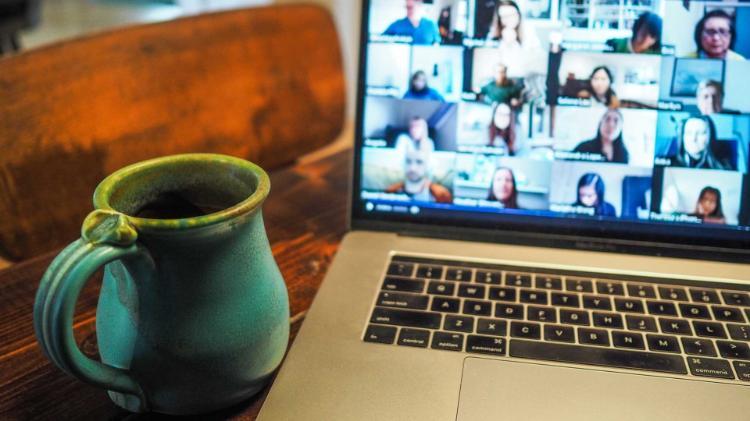 Coffee mug and laptop on dining room table. Laptop shows a webinar in progress