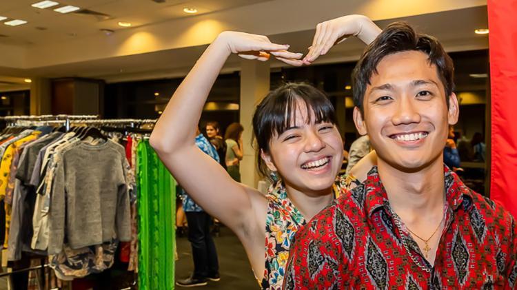 Two people looking happy nearby racks of clothing.