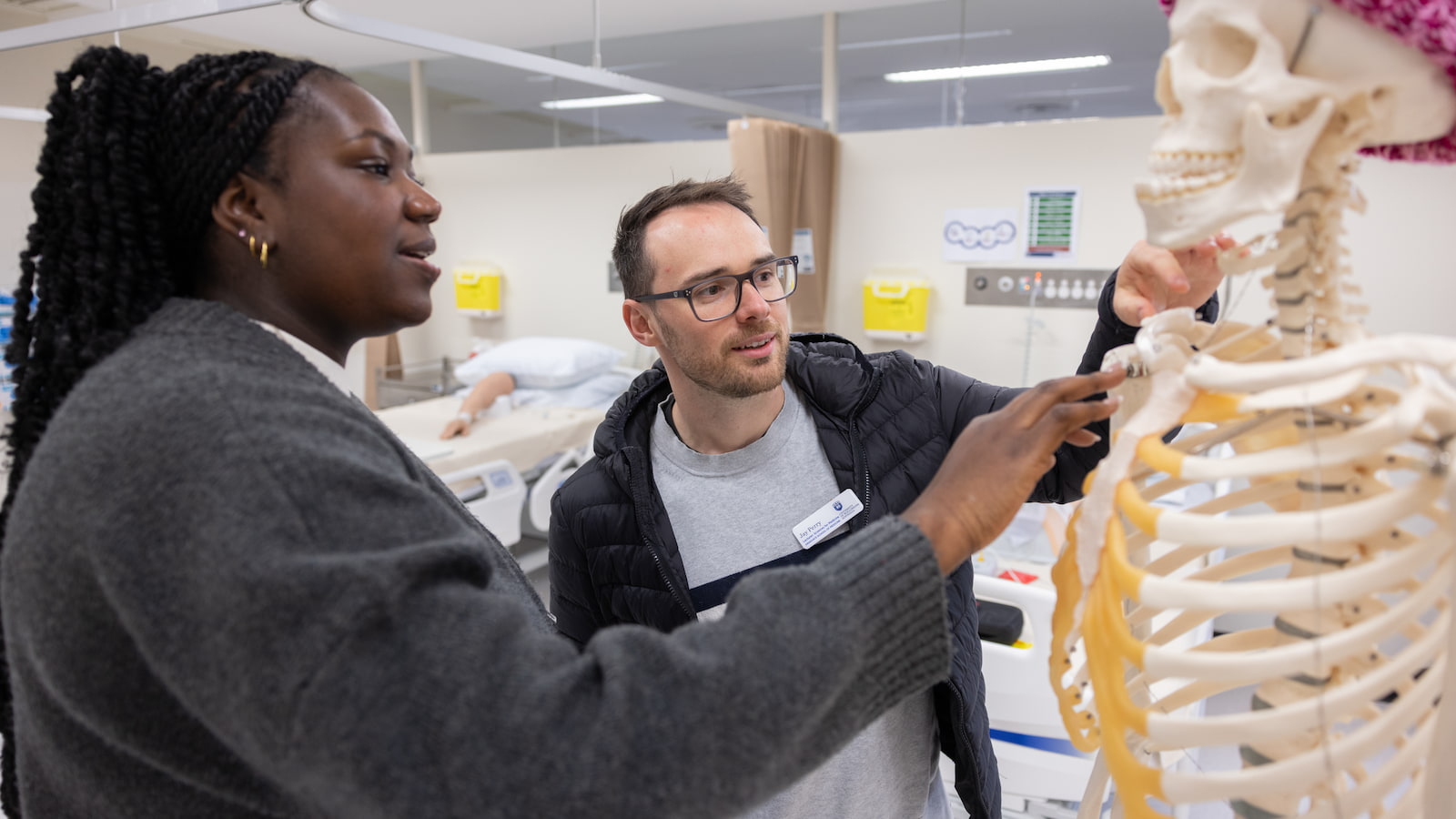 Two students look at a skeleton that is wearing a beanie. Photo: Mark Newsham
