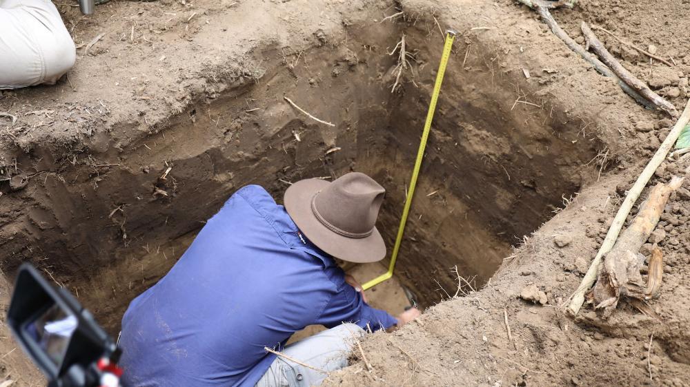 A man wearing an akubra hat digs in a trench in bushland. Photo: Rachel Pagitz – NSW Reconstruction Authority