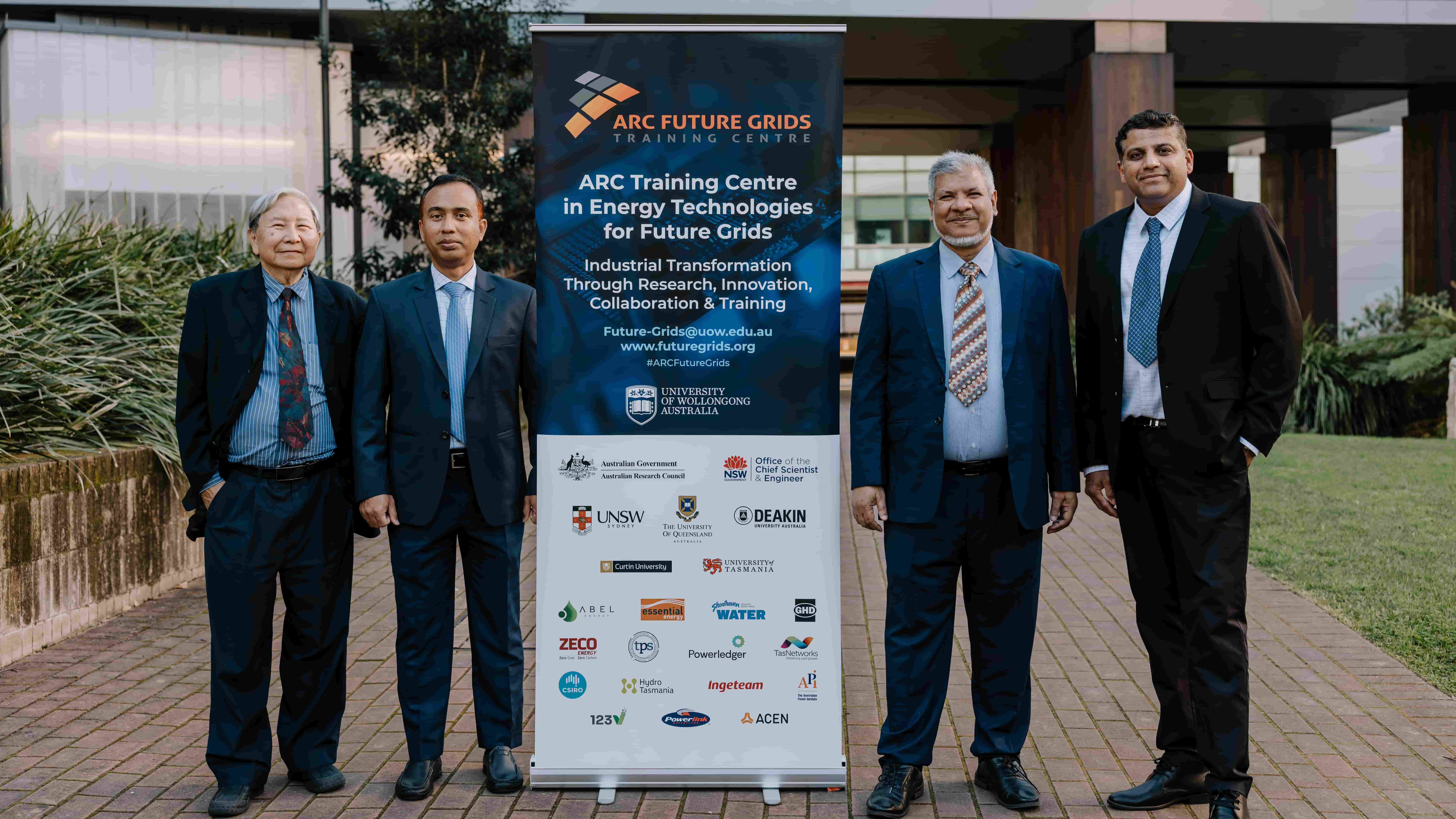 Four men -  Professor Danny Sutanto, Associate Professor Rabiul Islam, Distinguished Professor Kashem Muttaqi, and Associate Professor Ashish Agalgaonkar - wearing dark suits stand in a row outside the Molecular Horizons Building, with a banner for the ARC Future Grids Training Centre in the middle of the group. Photo: Michael Gray