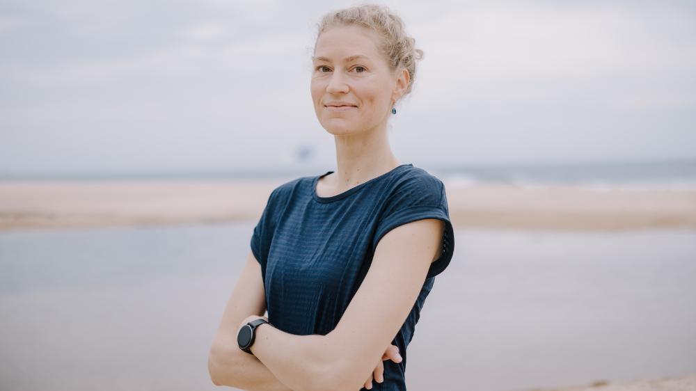 A woman stands at the beach with her arms folded. She is smiling. Photo: Michael Gray