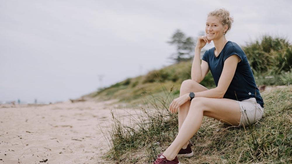 A woman sits in the sand dunes on the beach. She is smiling. Photo: Michael Gray