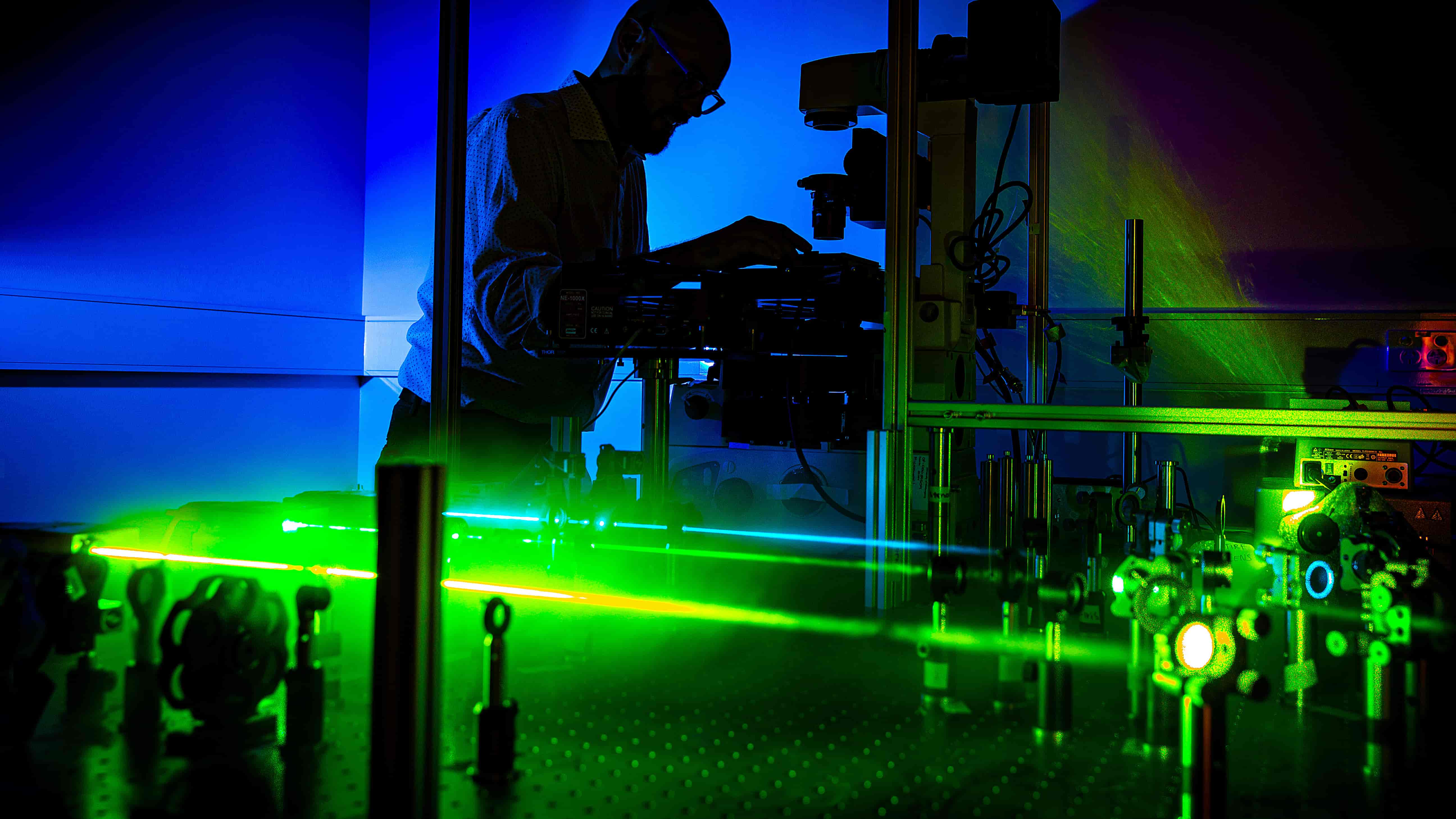 A man in profile uses a state-of-the-art microscope with blue and green colours in the background. Photo: Paul Jones