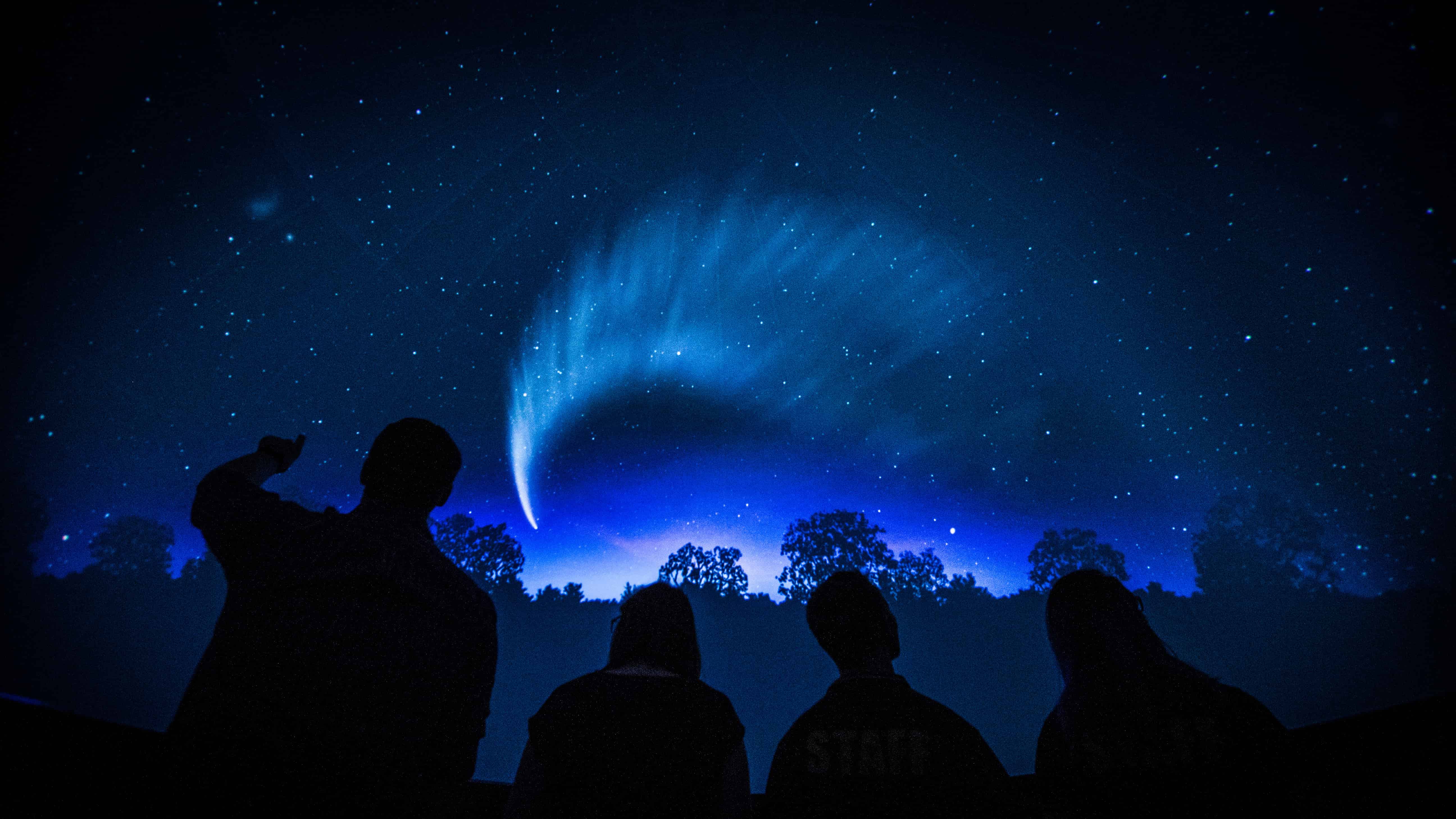 Four people are silhouetted against the background of the planetarium, which projects an image of stars and space. Photo: Paul Jones