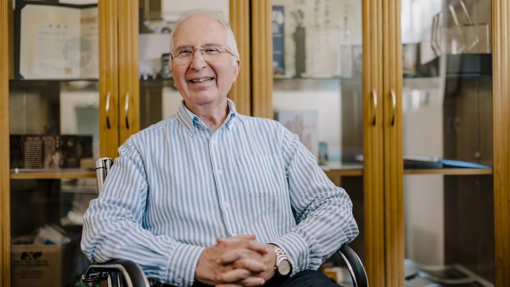 A man sits back in a chair with a smile in front of a set of shelves. Photo: Michael Gray