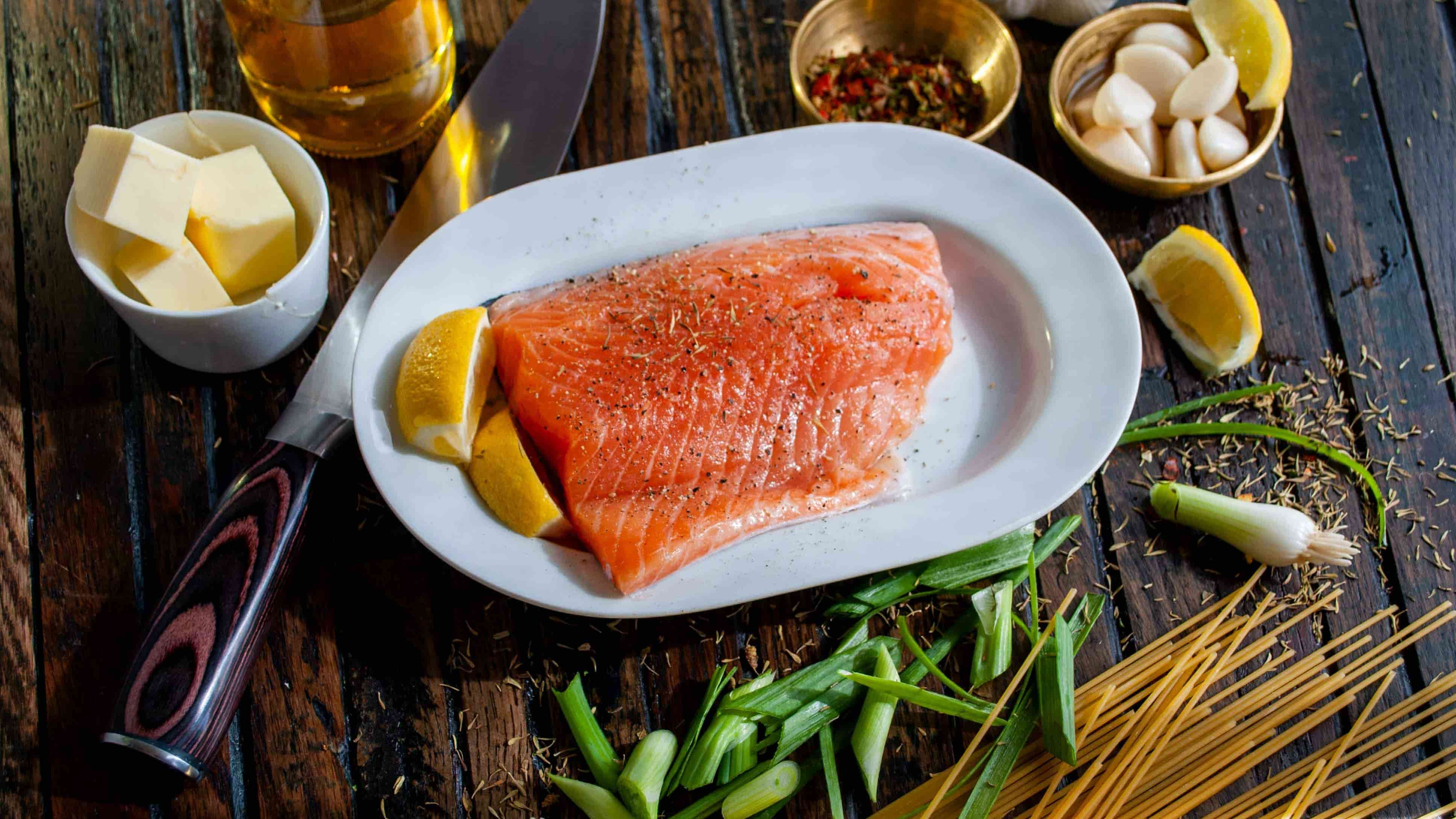 A plate of raw salmon, which is high in omega-3, is surrounded by bowls of garlic, lemon, butter and oil. Photo: David Townsend/Unsplash