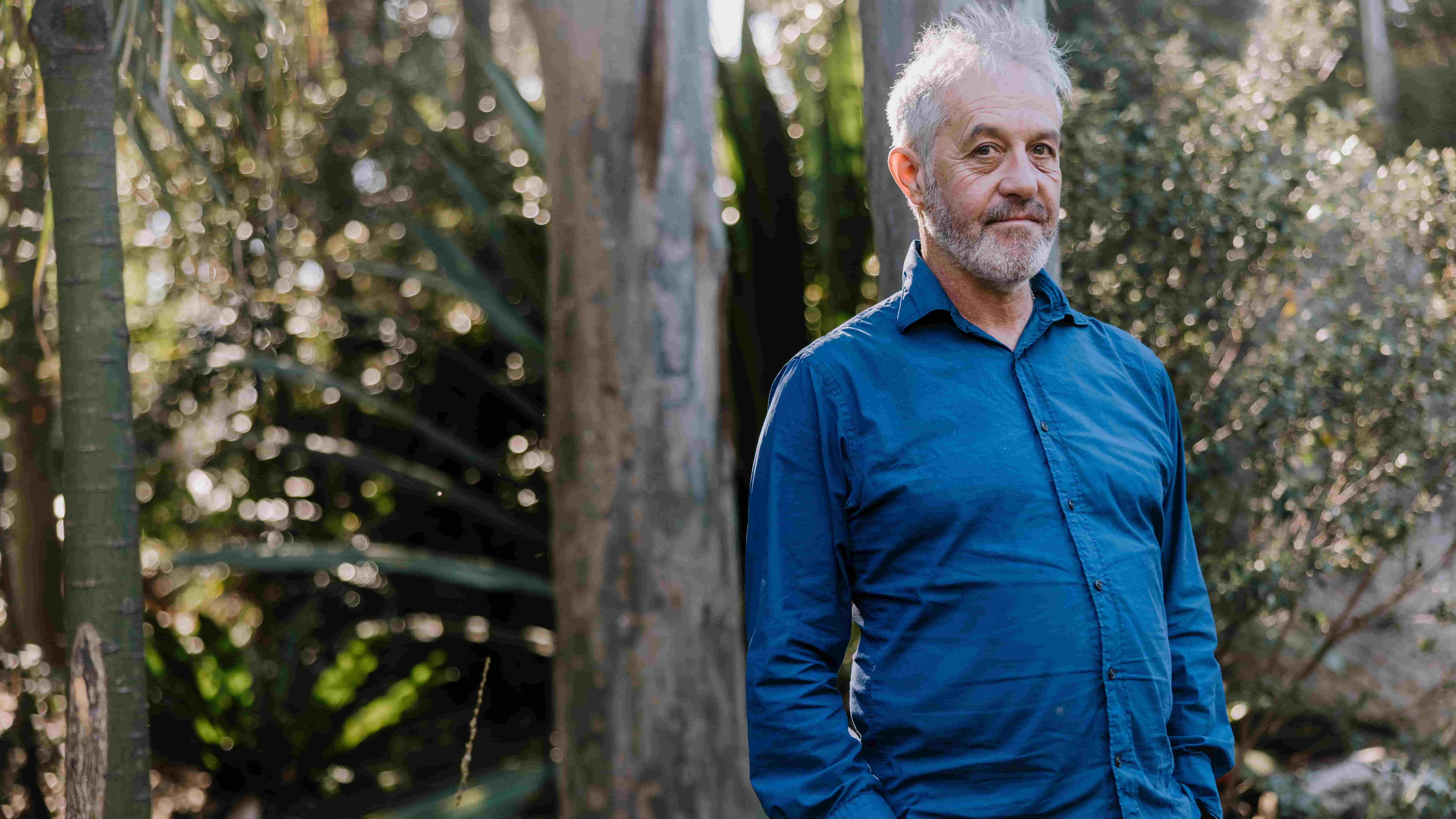 Associate Professor Owen Price wears a blue shirt with his arms crossed, standing in front of a tree. Photo: Michael Gray
