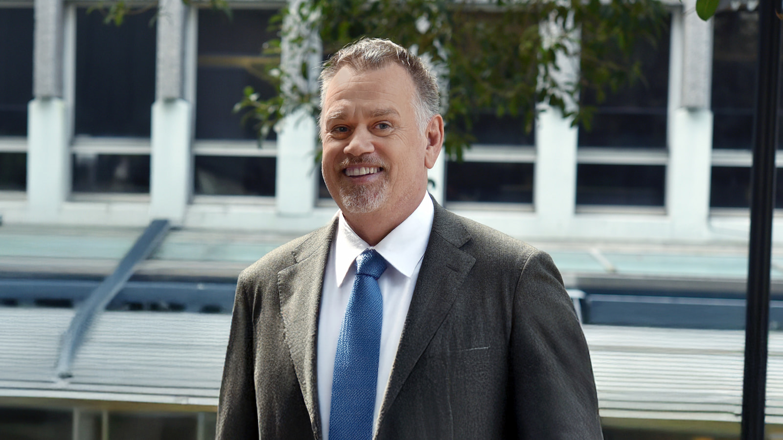 A profile image of a man wearing a suit and a blue tie with a smile on his face.