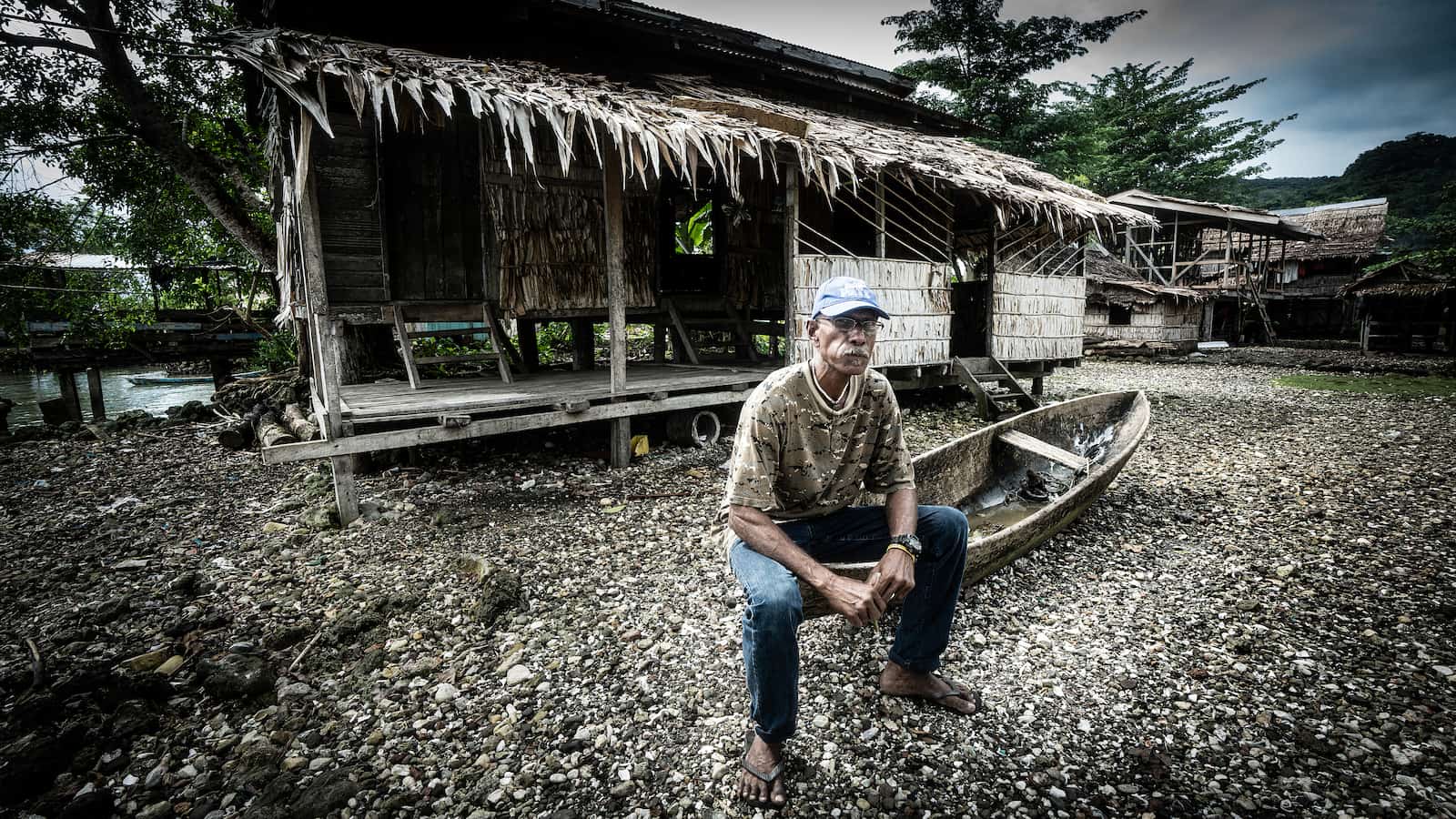 A man sits on an upturned canoe outside a small thatched cottage in a village in the Solomon Islands. Photo: Paul Jones