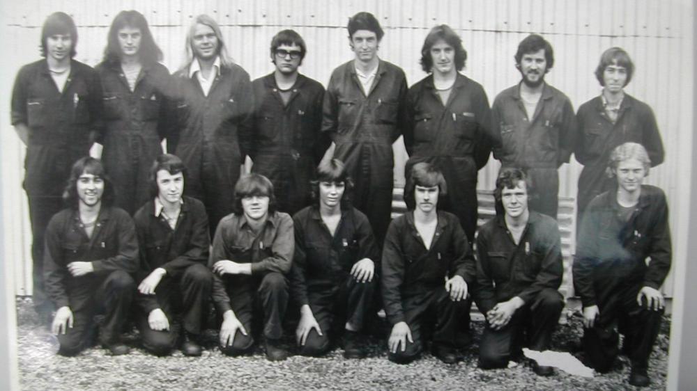A 1975 black and white photo of a group of young men in overalls smiling