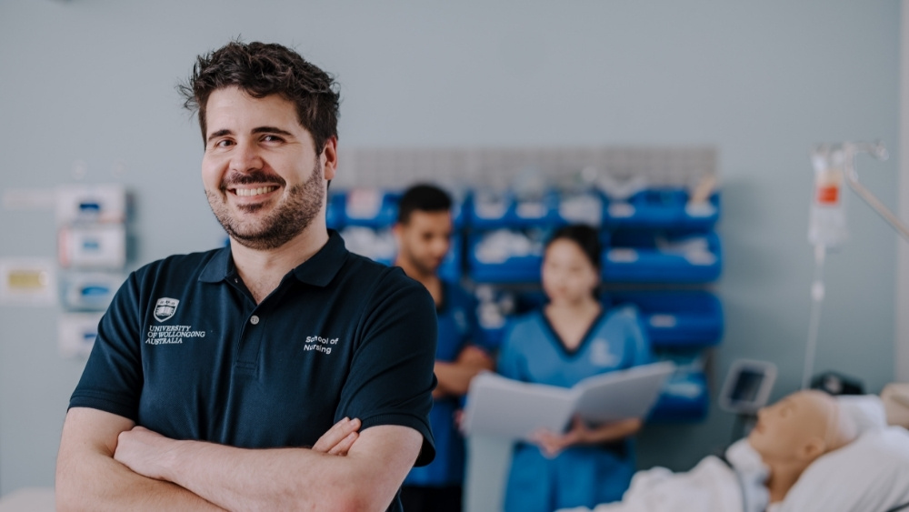 Brandon Smith, Registered Nurse and Associate Lecturer, School of Nursing, smiling at the camera with PhD nursing students in the background. Credit: Michael Gray