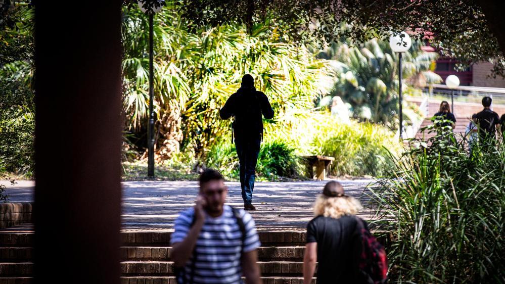 Students walking along a pathway under tress at the UOW Wollongong campus.