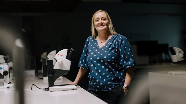 A woman stands in front of a series of microscopes in a dark laboratory. Photo: Michael Gray