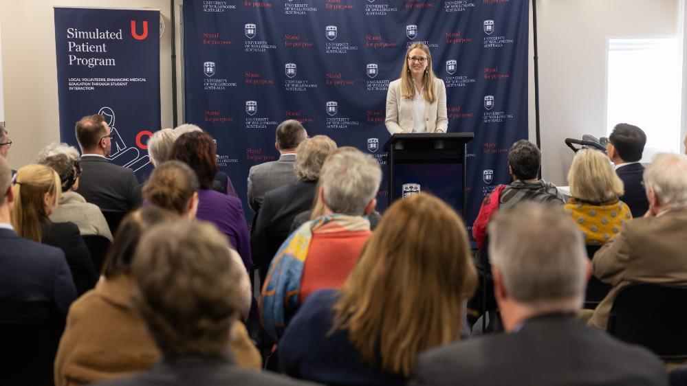A woman, Dr Taleitha Atkins, stands at a lectern addressing a large group of people. Photo: Mark Newsham