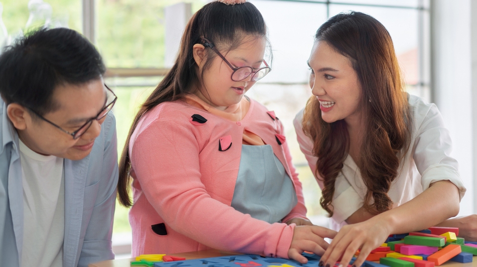 Happy father and mother playing education toy with their daughter down syndrome child in living room. Credit: Shutterstock ID 1913459575.