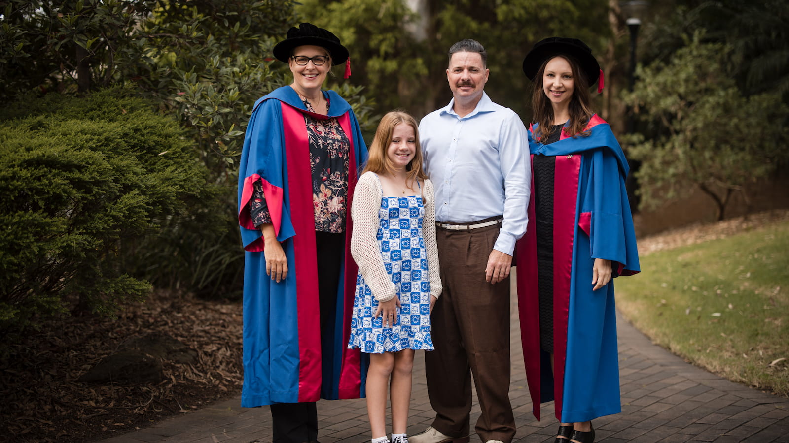 Michelle Eady, Grace Livingstone, Ben Livingstone and Bonnie Dean stand in a line at the Wollongong Campus. Michelle and Bonnie wear graduation gowns. Photo: Michael Gray