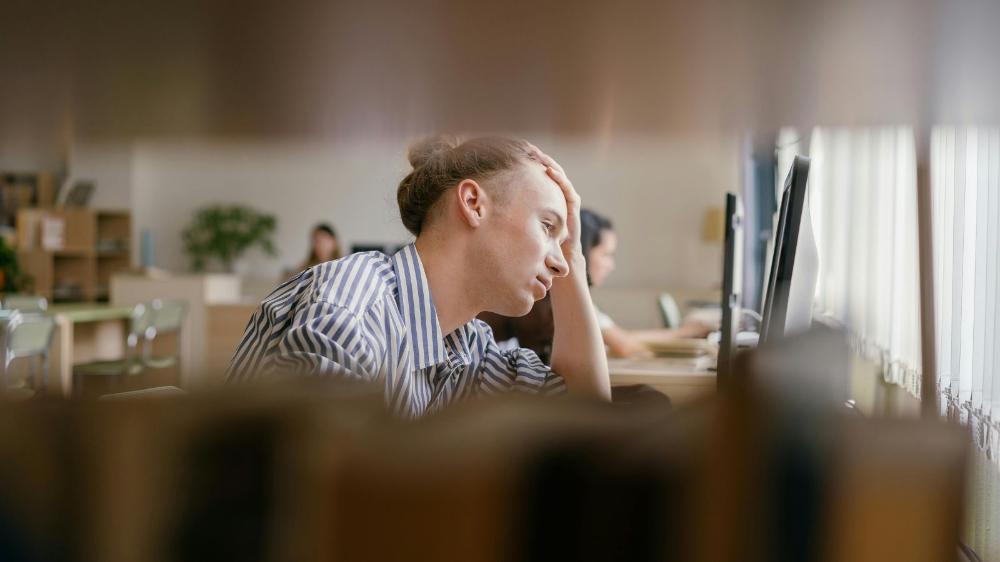 A students sits looking at a lap top with their head resting on their left hand