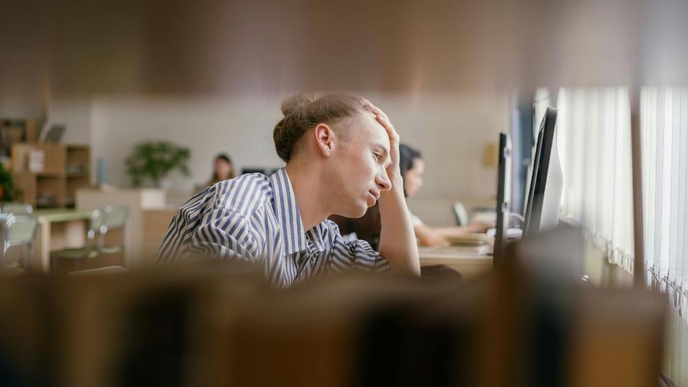 A students sits looking at a lap top with their head resting on their left hand