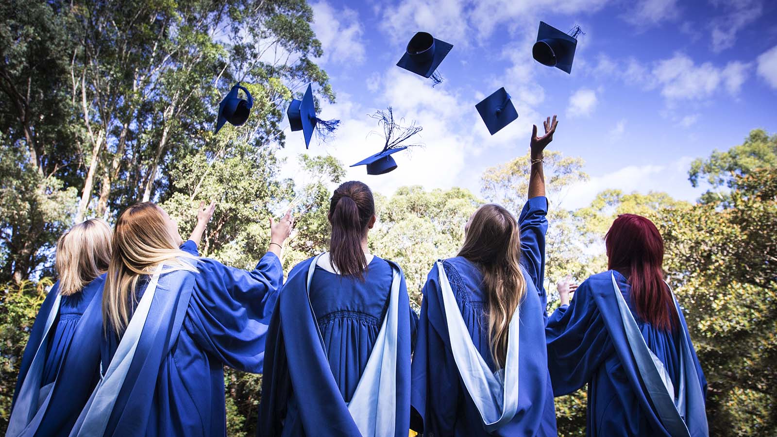 Newly graduated students in academic gowns throw their mortarboards in the air.