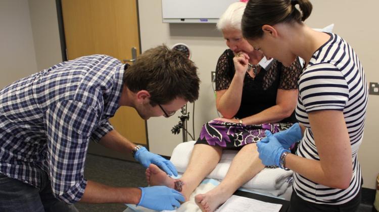 An older woman sits on a hospital bed while two trainee doctors tend to her foot. Photo: Supplied