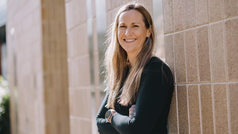 Dr Haidee Cadd leans against a brick wall. She has her arms folded, wears a black top and is smiling. Photo: Michael Gray