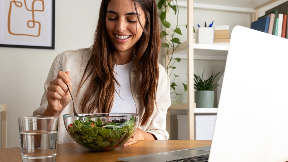 A woman eating healthy salad for lunch while working with laptop at home. Shutterstock: Daniel Hoz. ID 2375468073