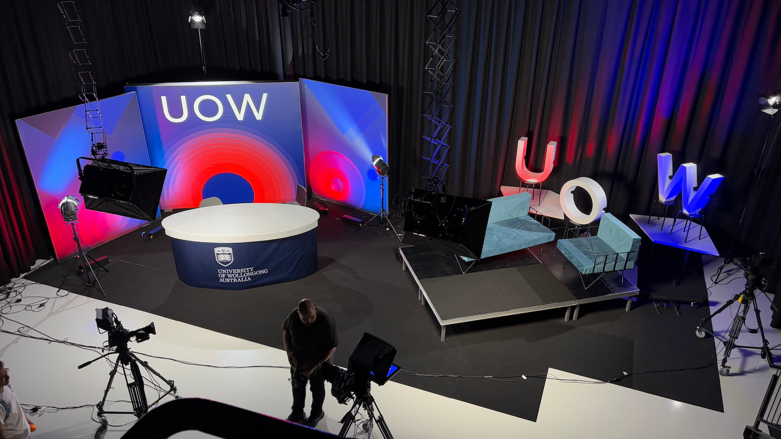 The broadcast set, with a large UOW letters in red, blue and white, on a black soundstage.