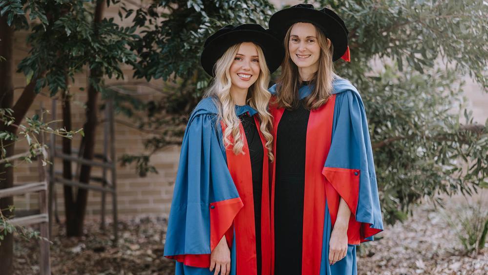 Emma James and Danielle Warren in academic dress to celebrate their graduation.