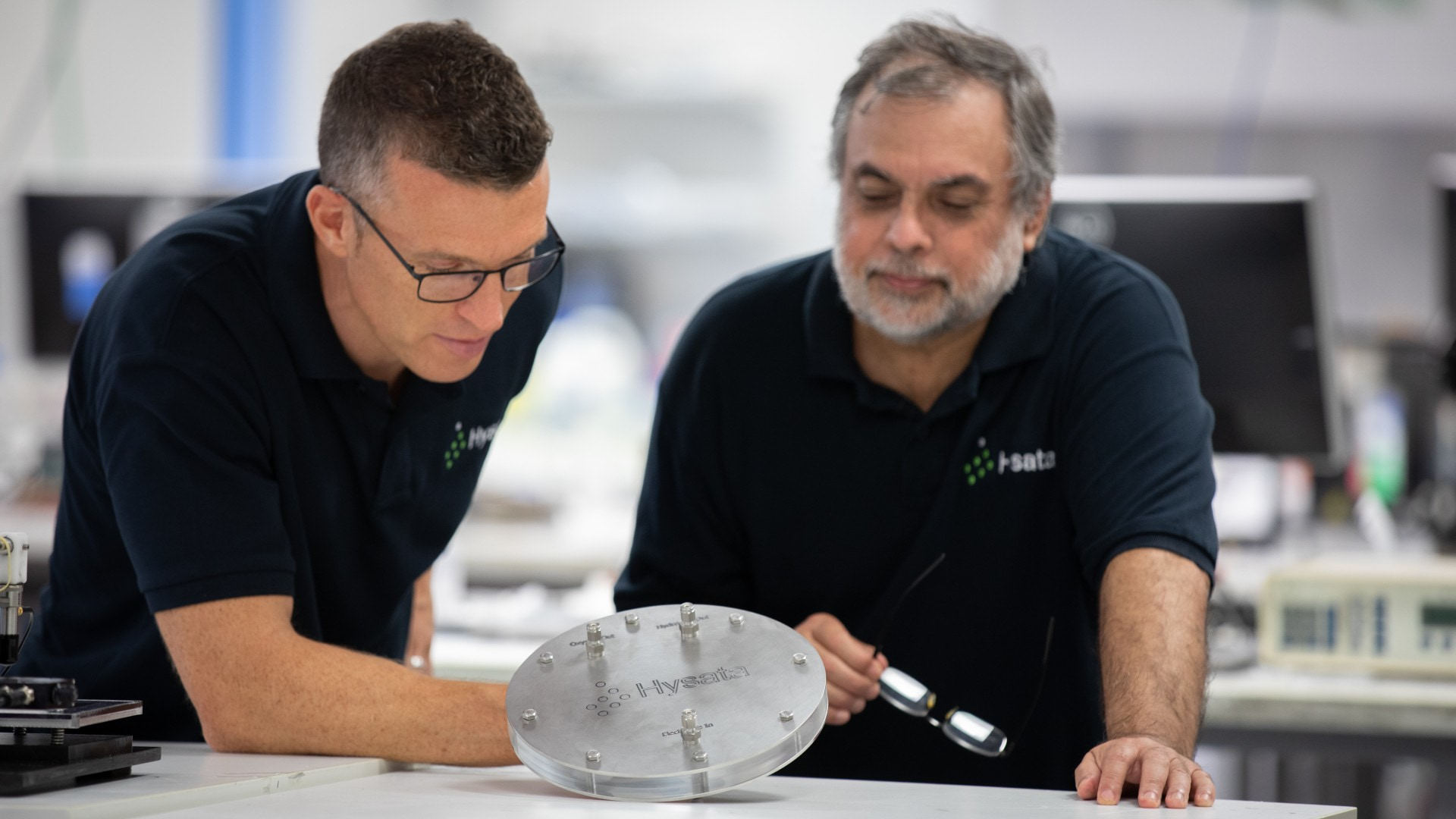 Dr Paul Barrett, CEO of Hysata, with Dr Gerry Swiegers, Chief Technical Officer at Hysata. They are in a lab wearing navy blue Hysata shirts.