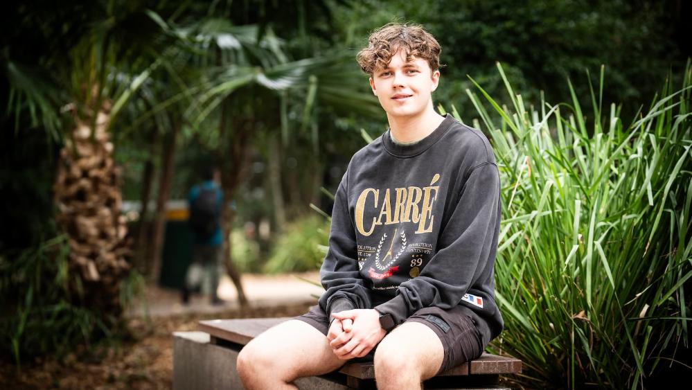 Jack Lenihan, wearing all black clothes, sits on a bench at Wollongong campus. Photo: Paul Jones