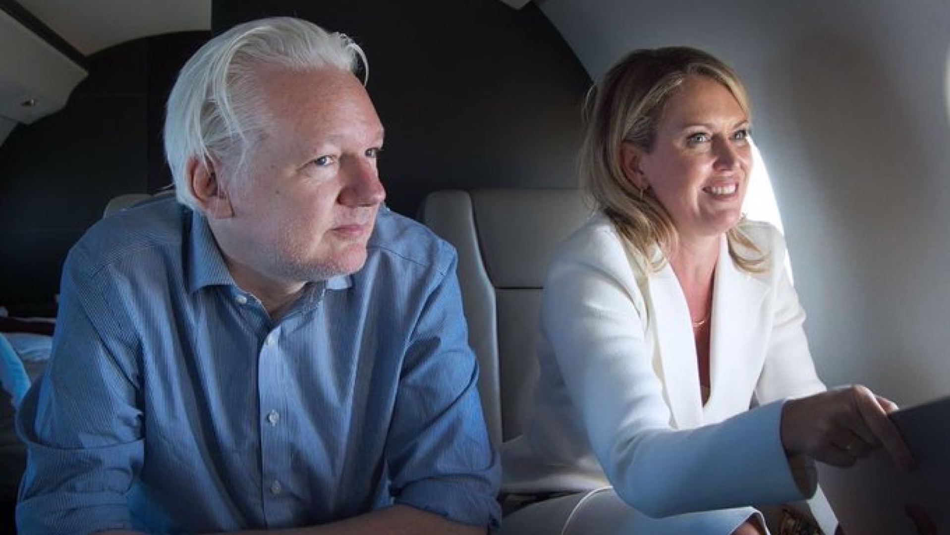 Julian Assange and Jennifer Robinson siting and smiling in a plane